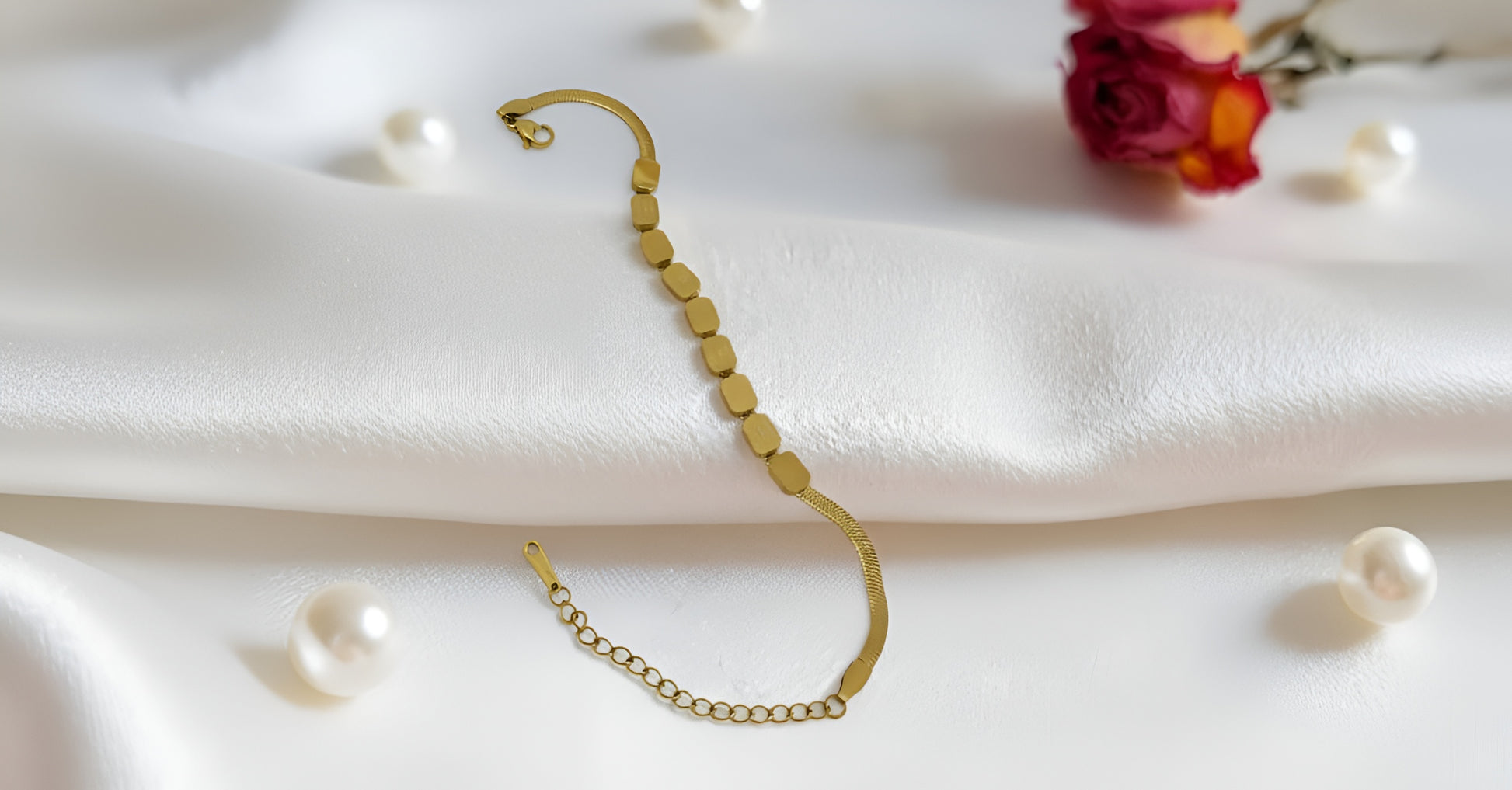 Gold bracelet on a white fabric background with pearls and flowers.