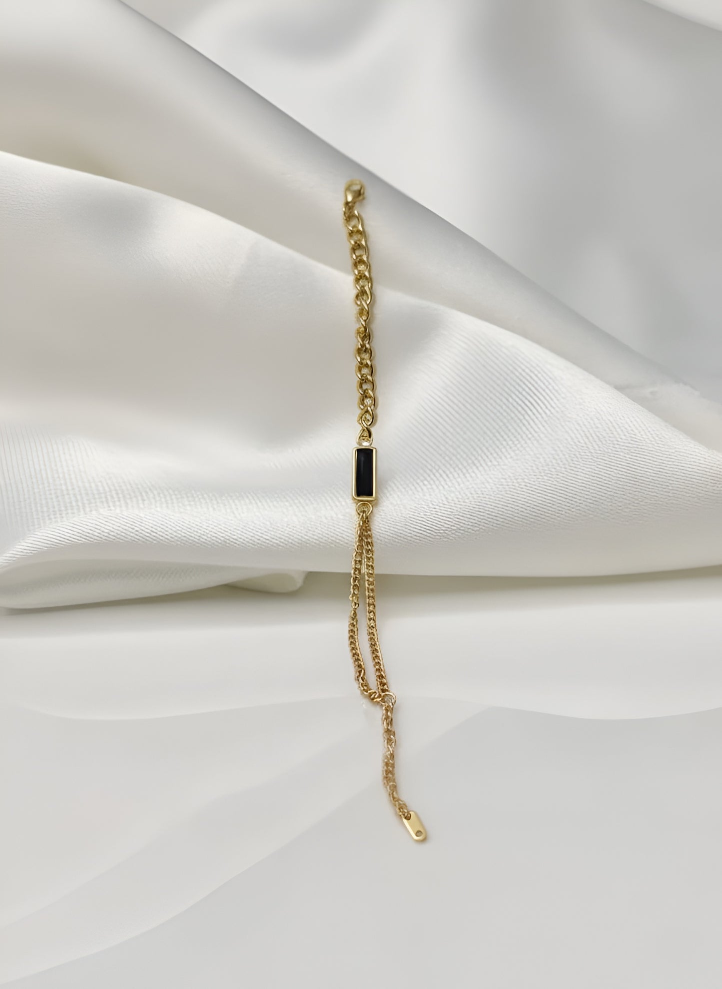 Gold bracelet with a black stone on a white fabric background
