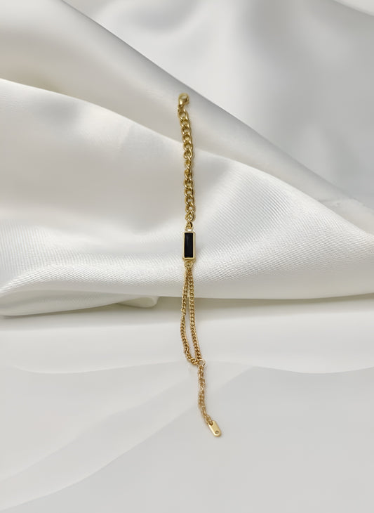 Gold bracelet with a black stone on a white fabric background